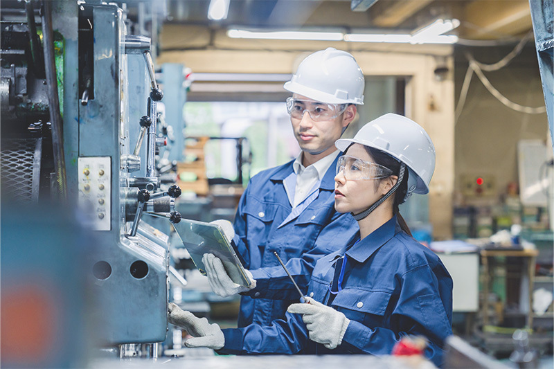 機械の前で確認している作業着姿の人々