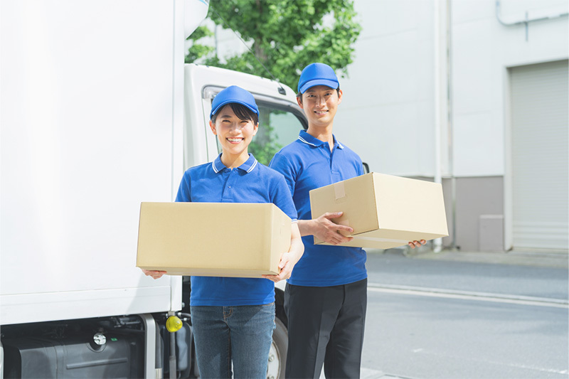 トラックの前で荷物を持って微笑む作業着姿の男女